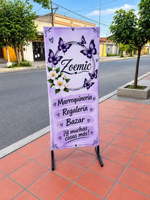 Banner vertical con pie apoyado en una vereda que anuncia una marroquinería, regalería y bazar