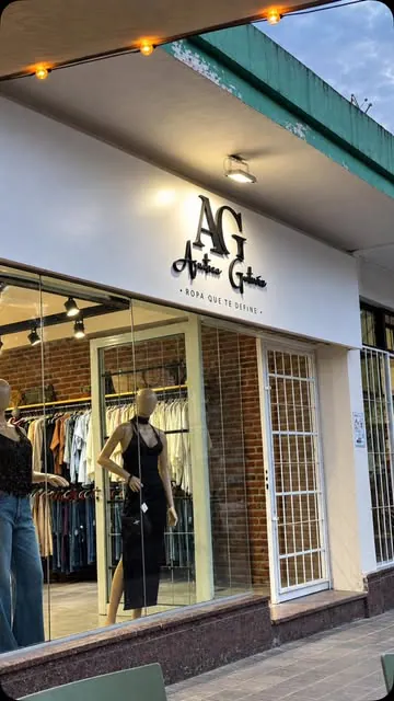 Frente de una boutique de ropa con logo y eslogan en letras corpóreas negras sobre un panel blanco
