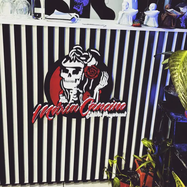 Logo con una calavera en capas de colores y letras corpóreas rojas y blancas sobre una pared de listones blancos y negros